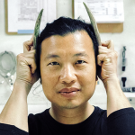 Tattfoo Tan in studio, smiling at the camera playfully holding two antlers next to their ears
