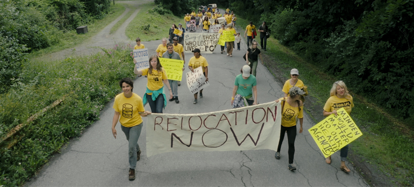 A group of marchers wears yellow shirts and protests through a rural community.