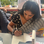 South Asian Female writer signing a book at a cafe.