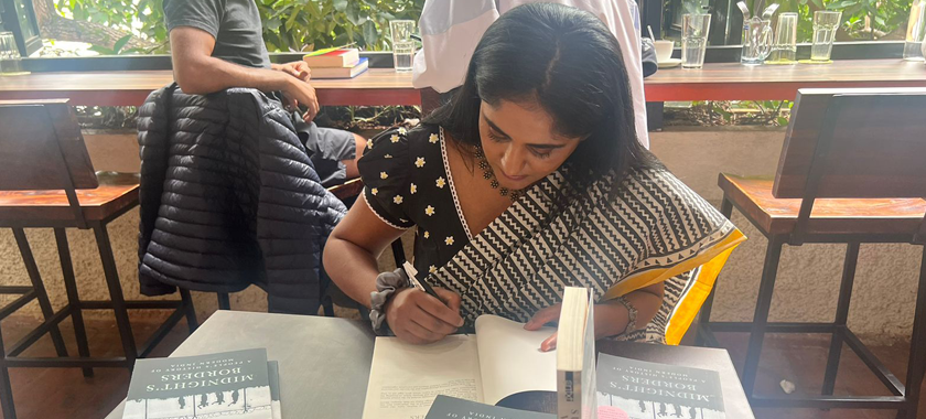 South Asian Female writer signing a book at a cafe.