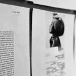 A close-up black and white photograph of several pages of poetry mounted on corkboard on the wall during a round of revisions, the pages are white with black text and some are blurred out from view