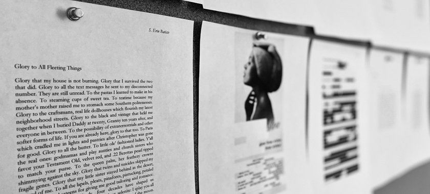 A close-up black and white photograph of several pages of poetry mounted on corkboard on the wall during a round of revisions, the pages are white with black text and some are blurred out from view