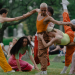 Six dancers perform at Green-Wood Cemetery in Brooklyn, a seated crowd and headstones behind them.