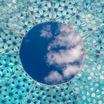 A blue sky with a few whispy white clouds can be seen through a small circle that is the top of a blue patterned Dome Oculus.