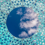 A blue sky with a few whispy white clouds can be seen through a small circle that is the top of a blue patterned Dome Oculus.
