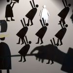Shadowy papercraft figurines dance and play instruments while a large blurred profile of a woman dominates the scene.