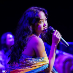 A performer singing off to the distance as three performers in the background, blurred, sit side by side.