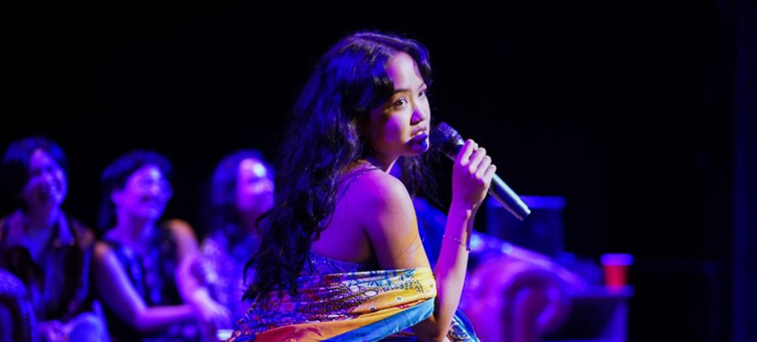 A performer singing off to the distance as three performers in the background, blurred, sit side by side.