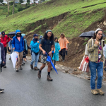 Photo taken in a rural and mountainous area in Puerto Rico, there is a landslide triggered by a road cut and heavy rain. People are walking up the road, observing the land falling.