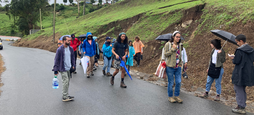 Photo taken in a rural and mountainous area in Puerto Rico, there is a landslide triggered by a road cut and heavy rain. People are walking up the road, observing the land falling.