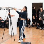 The artist performs with an indigenous blowgun from the Philippines. She is positioned in front of a live 3D scanner, which captures a 3D model of her head/arms, as she holds the blowgun to her mouth.