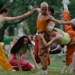 Six dancers perform at Green-Wood Cemetery in Brooklyn, a seated crowd and headstones behind them.