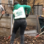 Four volunteers using shovels and pitchforks are processing compost in two metal bins.