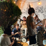 A film crew team is recording a live painting concert with 4 musicians and 1 visual artist in a backyard during the night