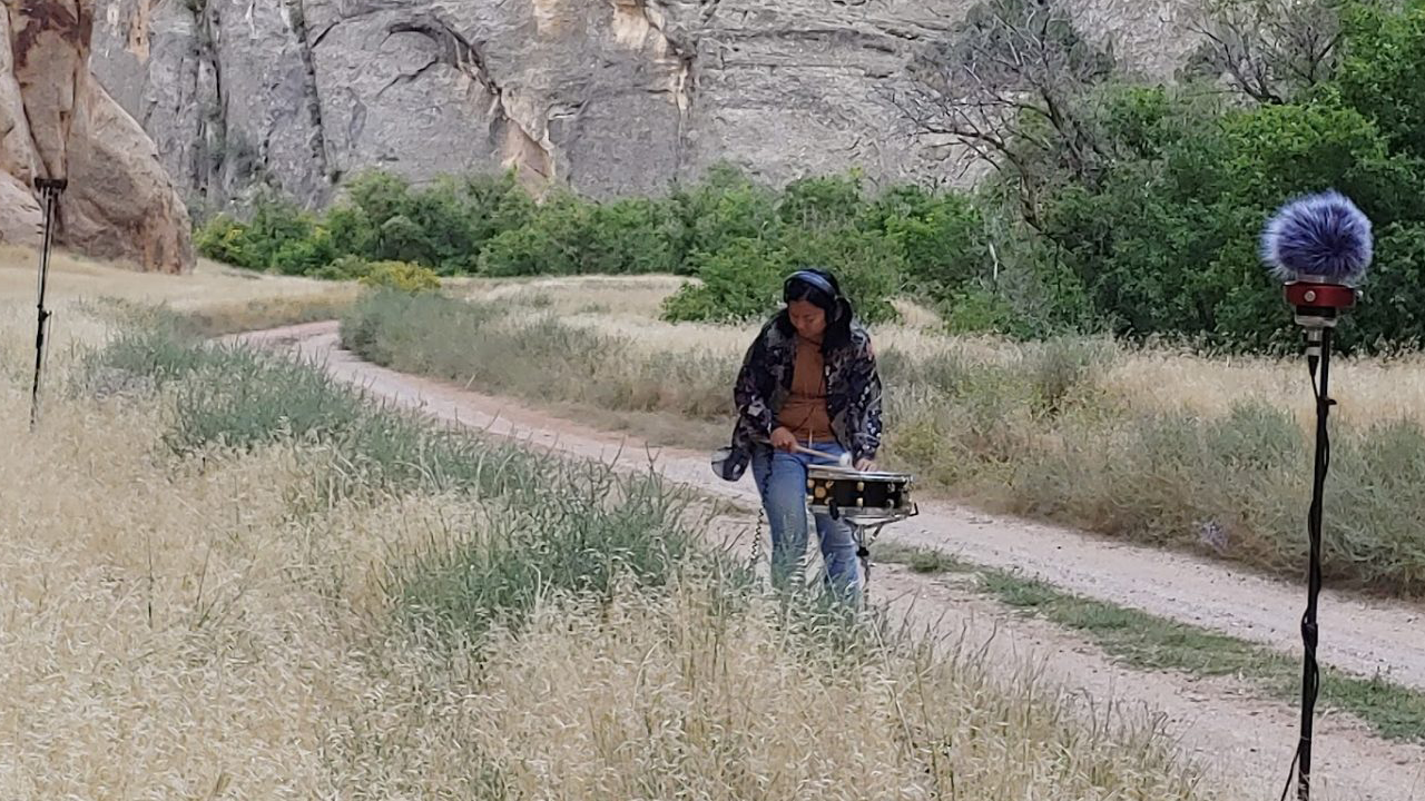 Pilipinx woman percussionist recording a snare in the echos of a canyon at Dinosaur Monument Park in Colorado and Utah border.