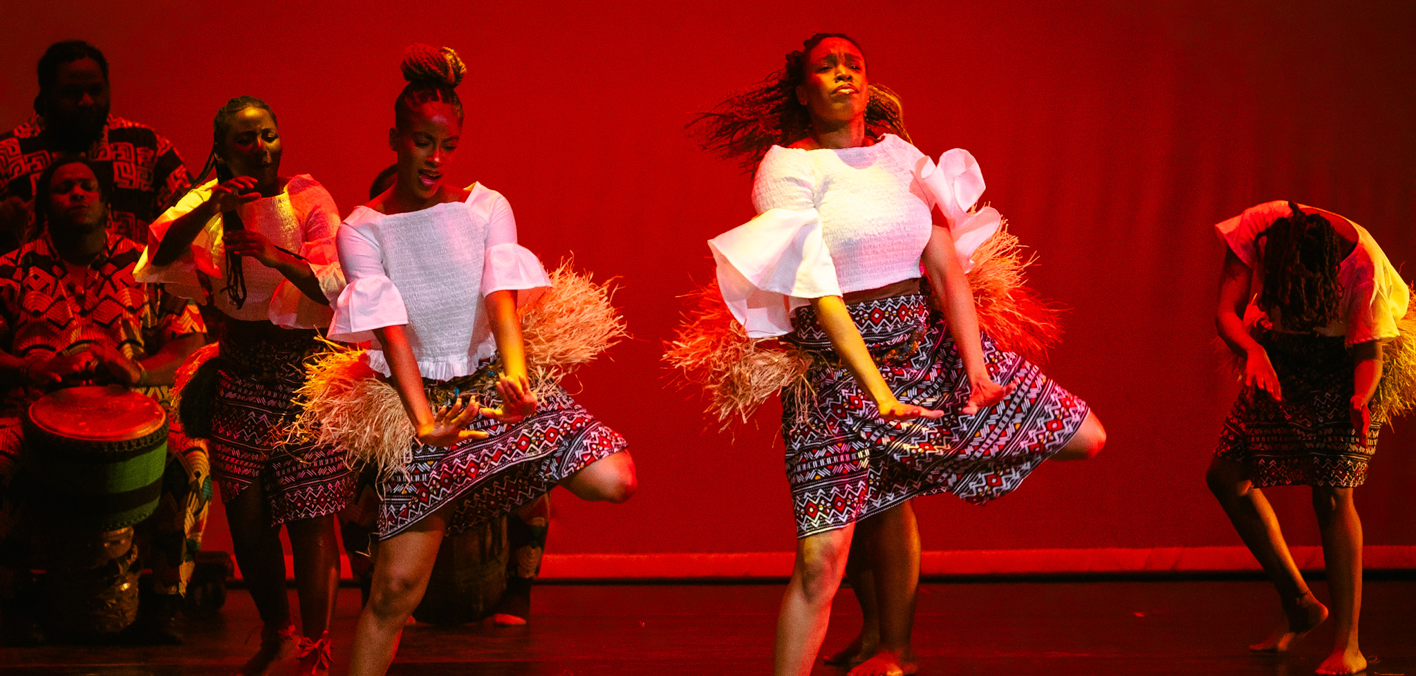 Two women performing on stage with drummers playing.