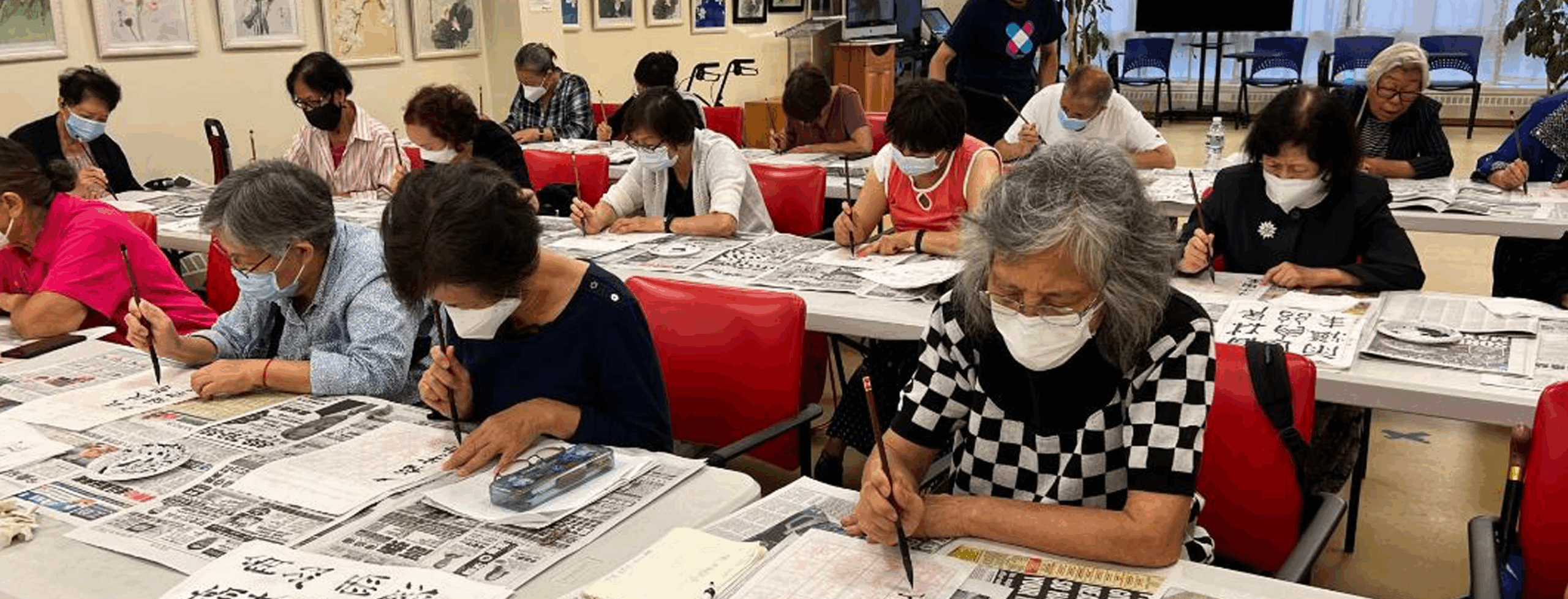 A room of older people concentrating and doing calligraphy.