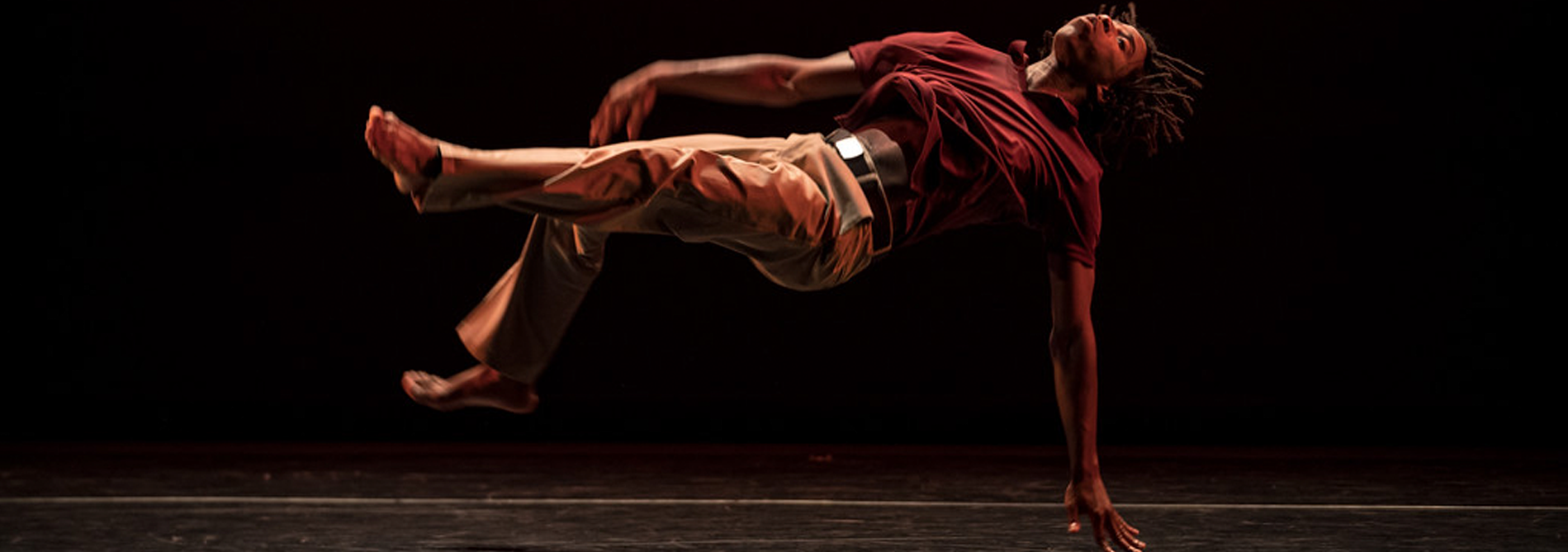 Cameron McKinney, wearing a red polo and long khaki pants, pushes himself from the floor, floating in midair with his head tilted back.