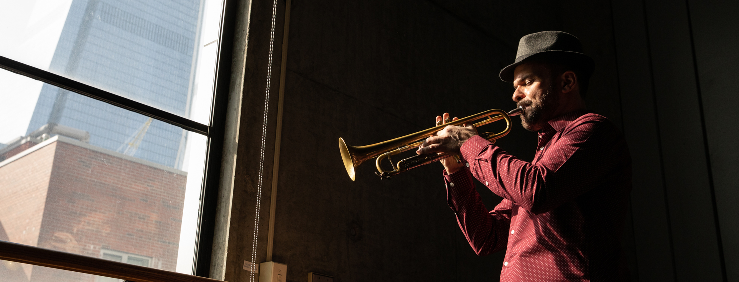 Amir ElSaffar playing his trumpet, dramatically lit near a window