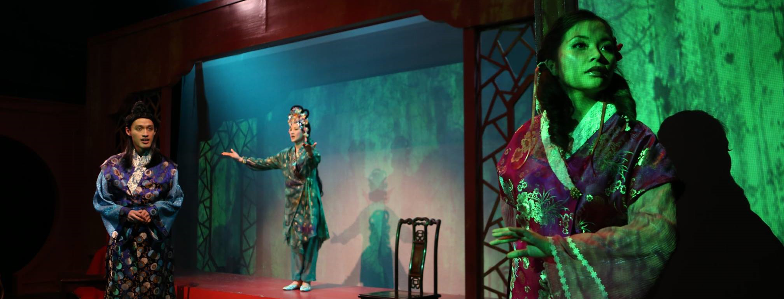 Three figures dressed in classical Chinese costumes, bathed in multi-coloured light: a pair of young lovers, and in the background a fairy holding out her arms.