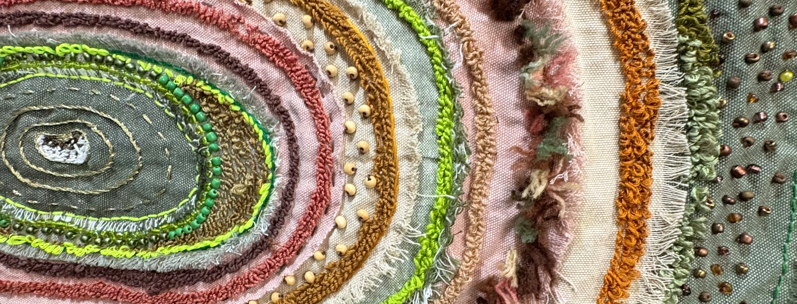 Textile artwork with intricate beading and sewing; with a center oval shape with rings of other colors and fabrics extending out