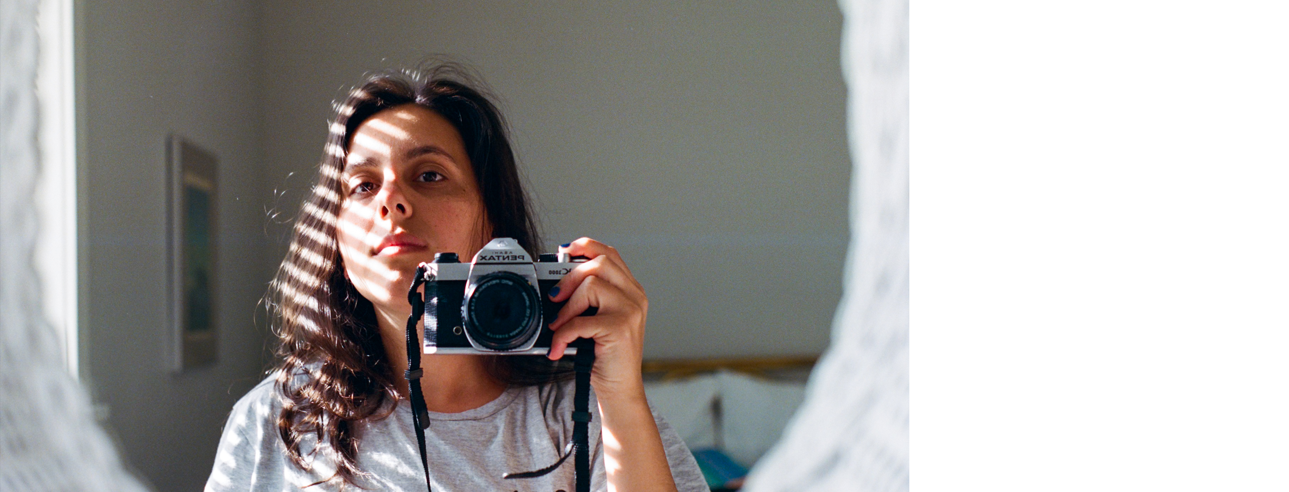 Mei Seva photographed reflecting in a mirror, holding a camera