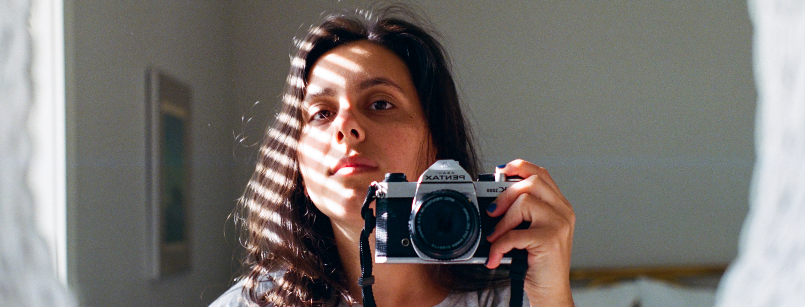 Mei Seva photographed reflecting in a mirror, holding a camera
