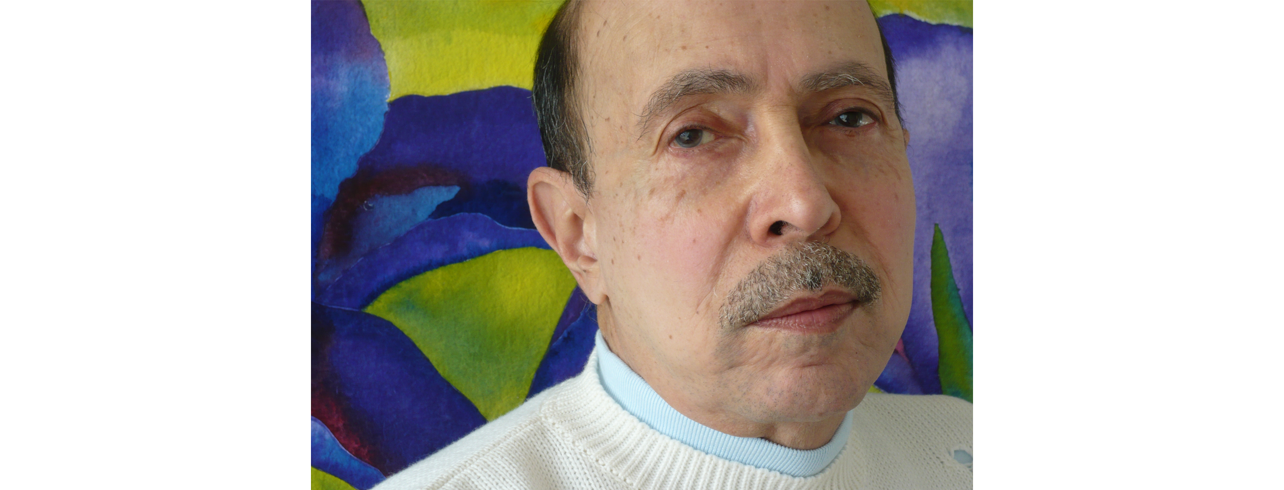 Close-up color photo of Basil Alkazzi in front of one of his vibrant paintings