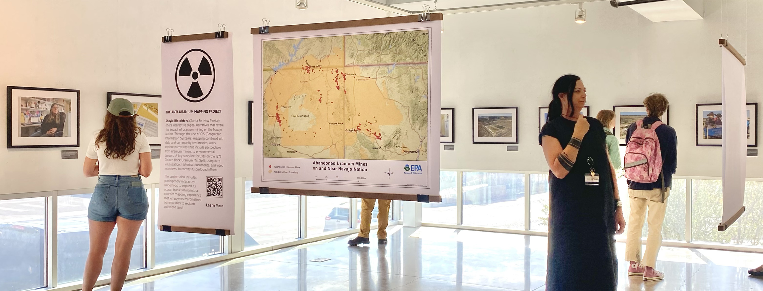 Students at an on campus gallery at the University of New Mexico observe the installation of photography images and suspended maps of abandoned uranium mines from the Anti Uranium Mapping Project.