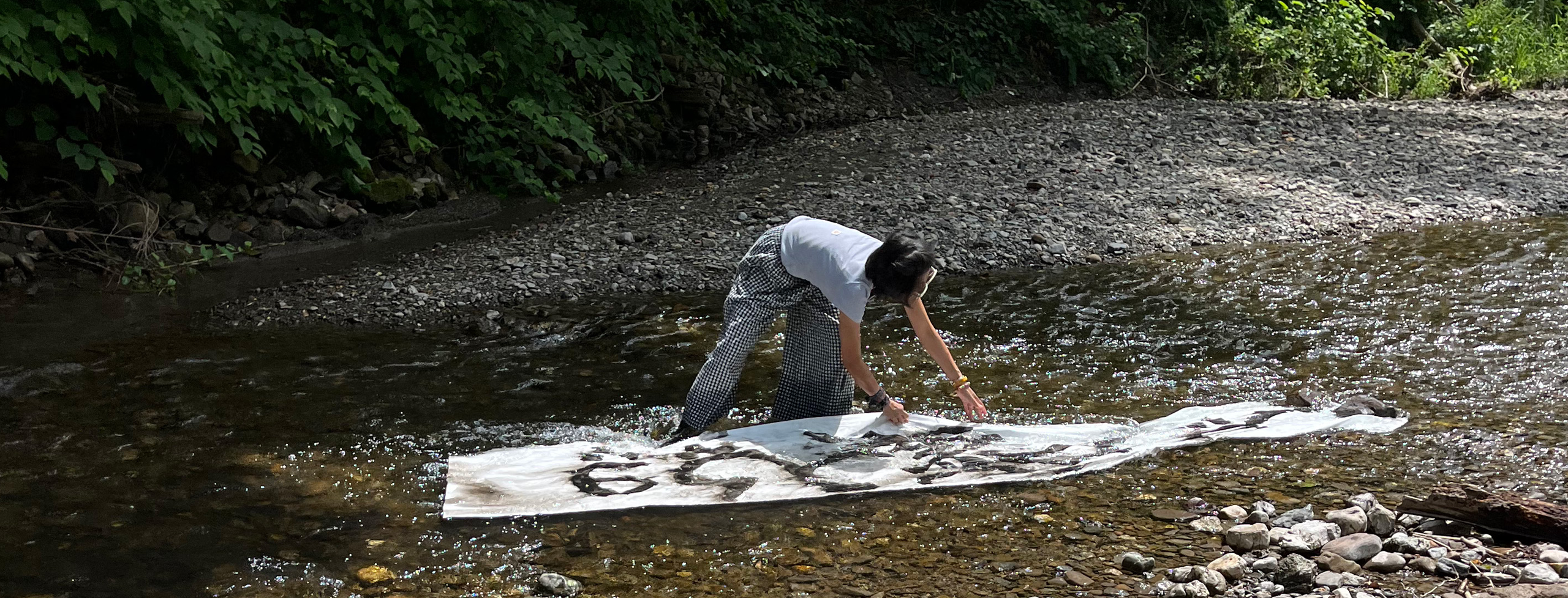 The artist arranging a calligraphy scroll in a shallow creek.