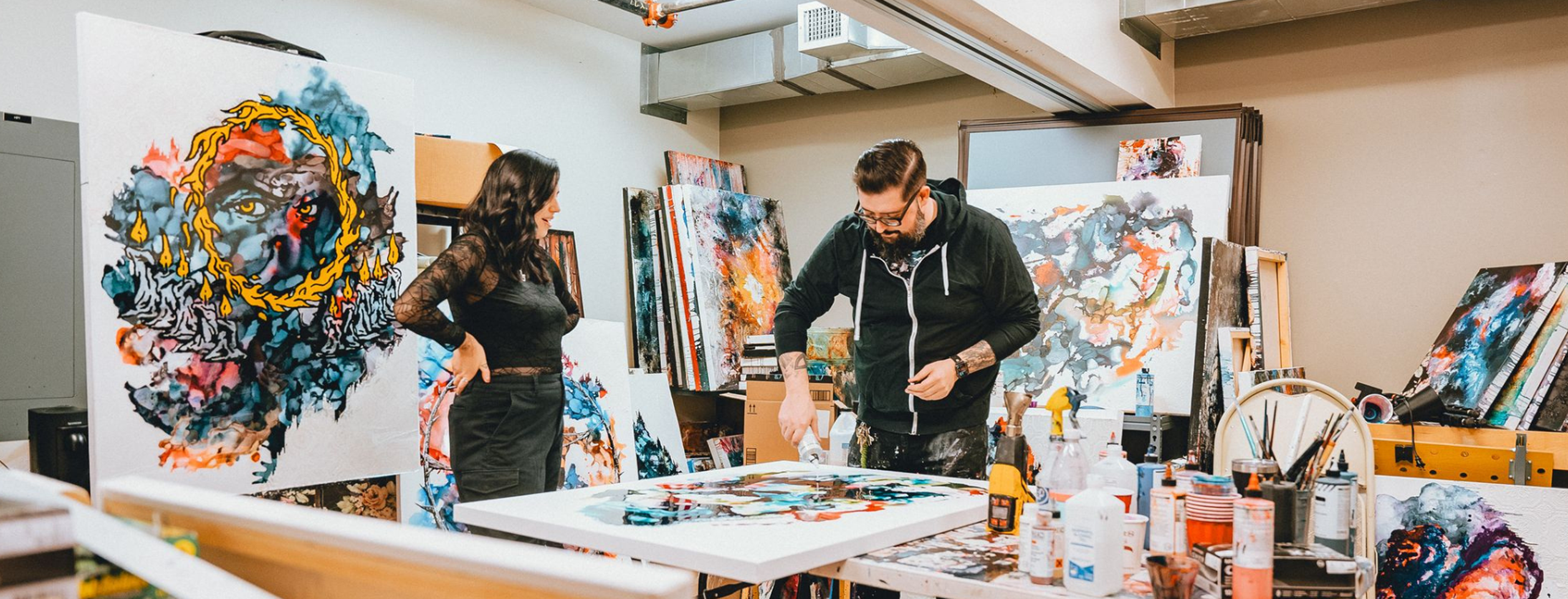 Two people in a painting studio, one pouring paint on a canvas