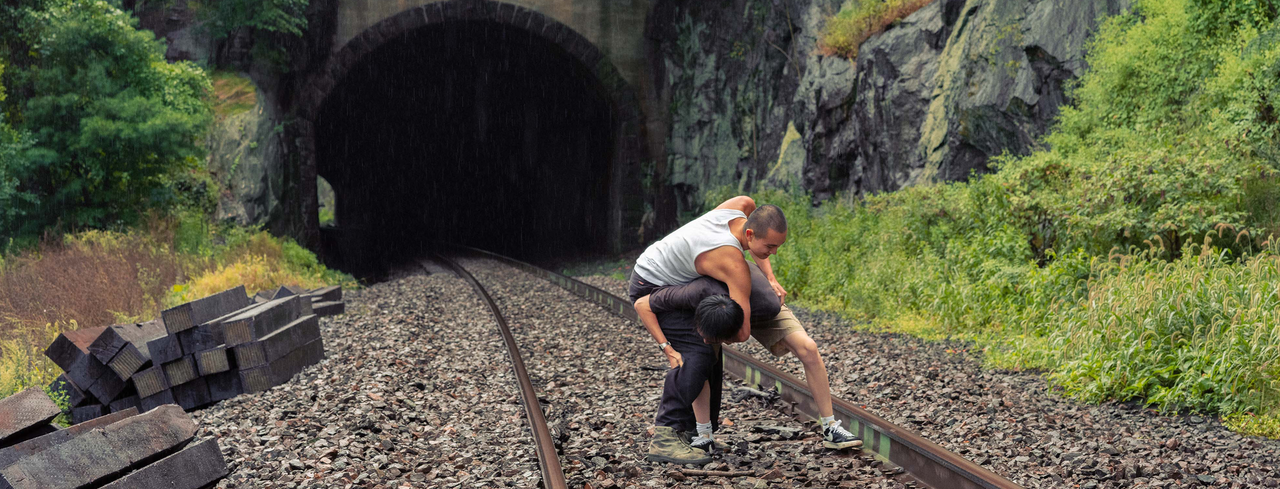 Two young men who are brothers are wrestling in the rain on railroad tracks in Hudson, NY