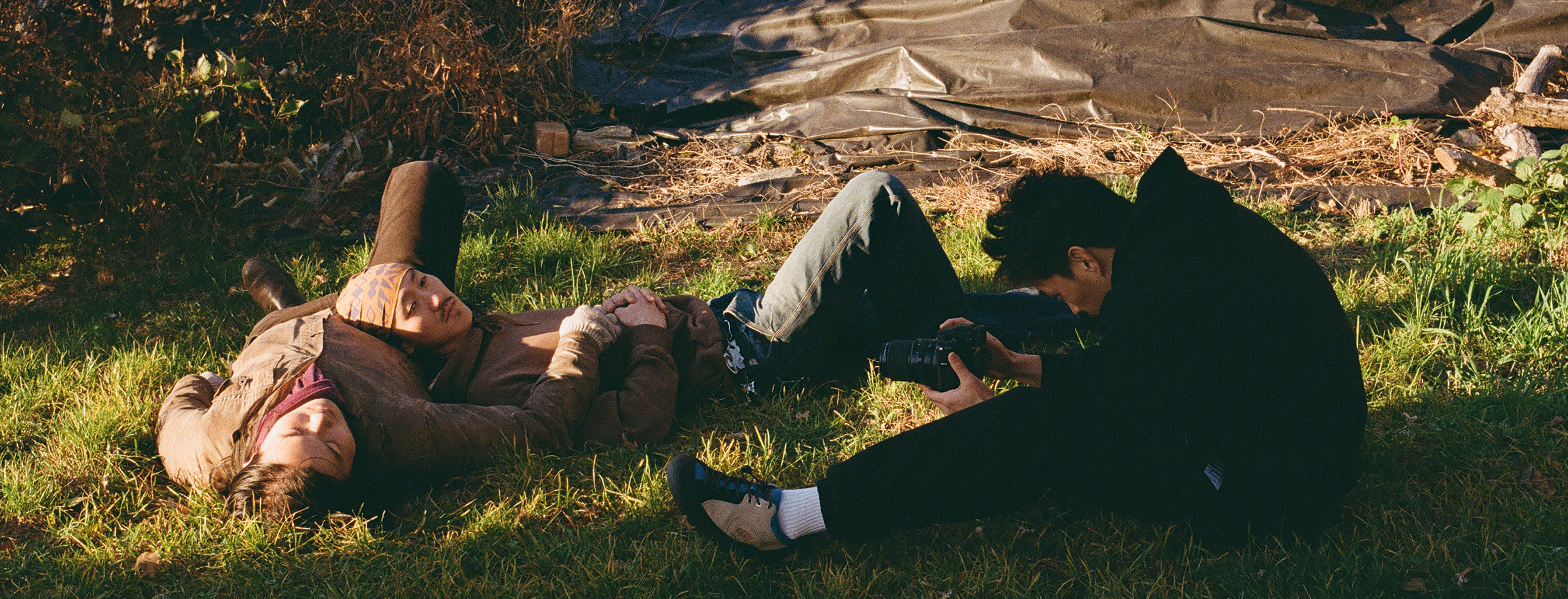 Andrew Kung on the ground with his camera, photographing an individual who is laying in the grass