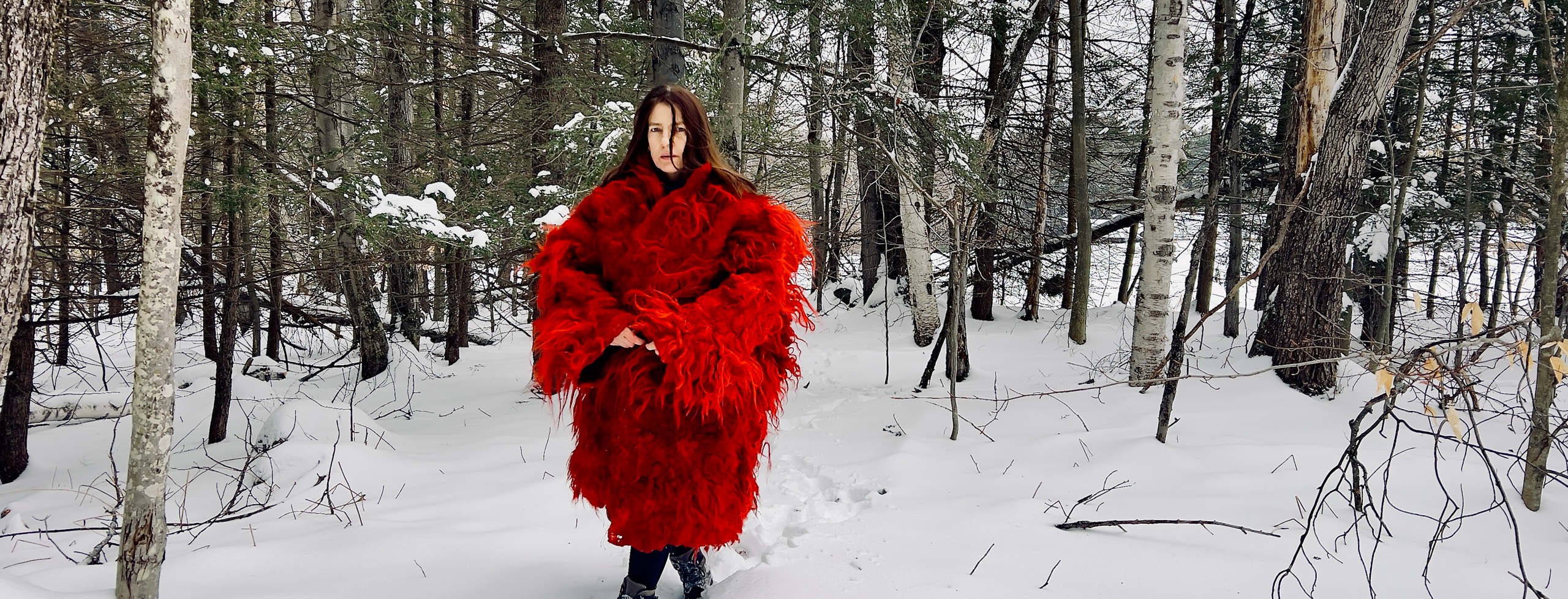 Brigitta Varadi wears a long bright red coat of fluffy wool, standing out against a winter backdrop of snow and trees