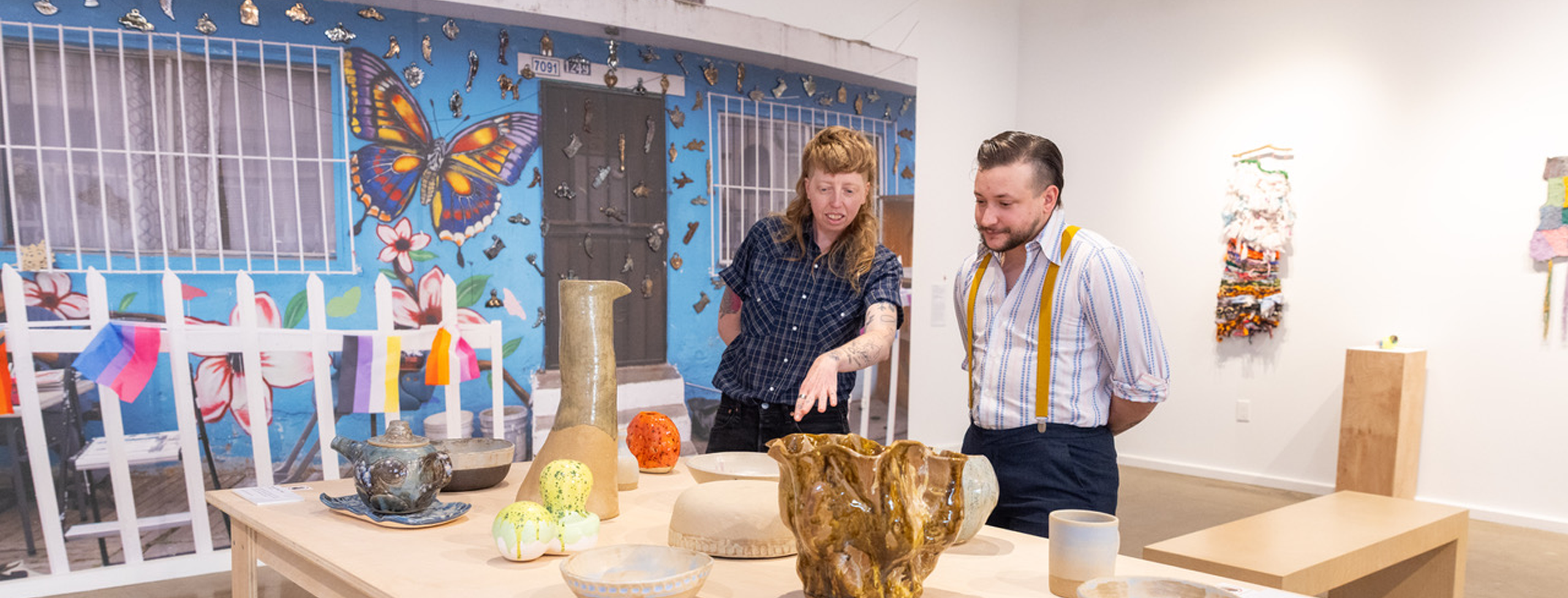 Installation view of "Craft-itarianism: Community Action Through Craft" exhibition featuring two people regarding ceramic artworks on a table
