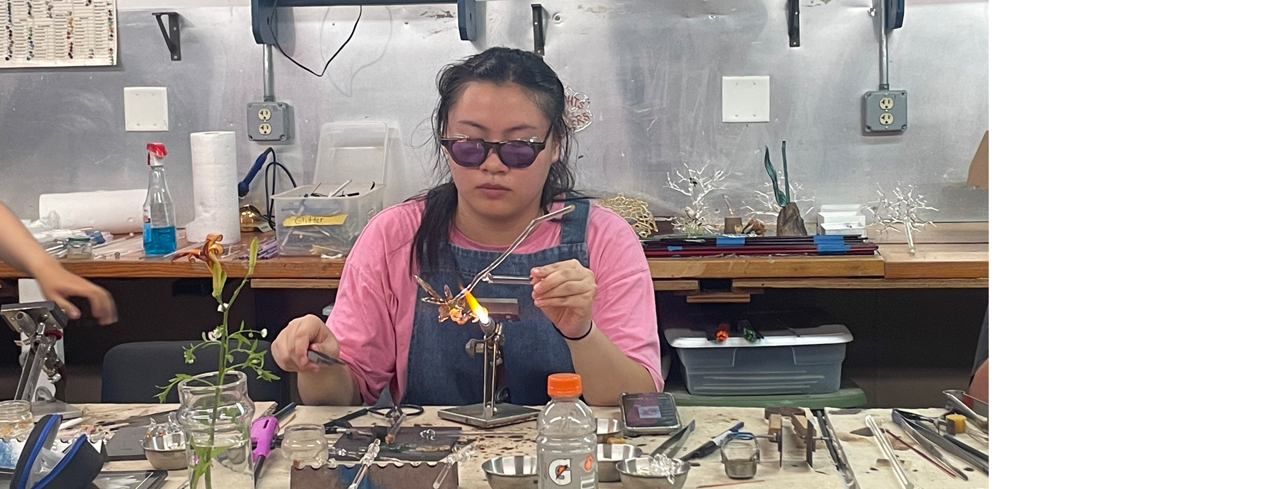 A student works with a flame in a glass studio